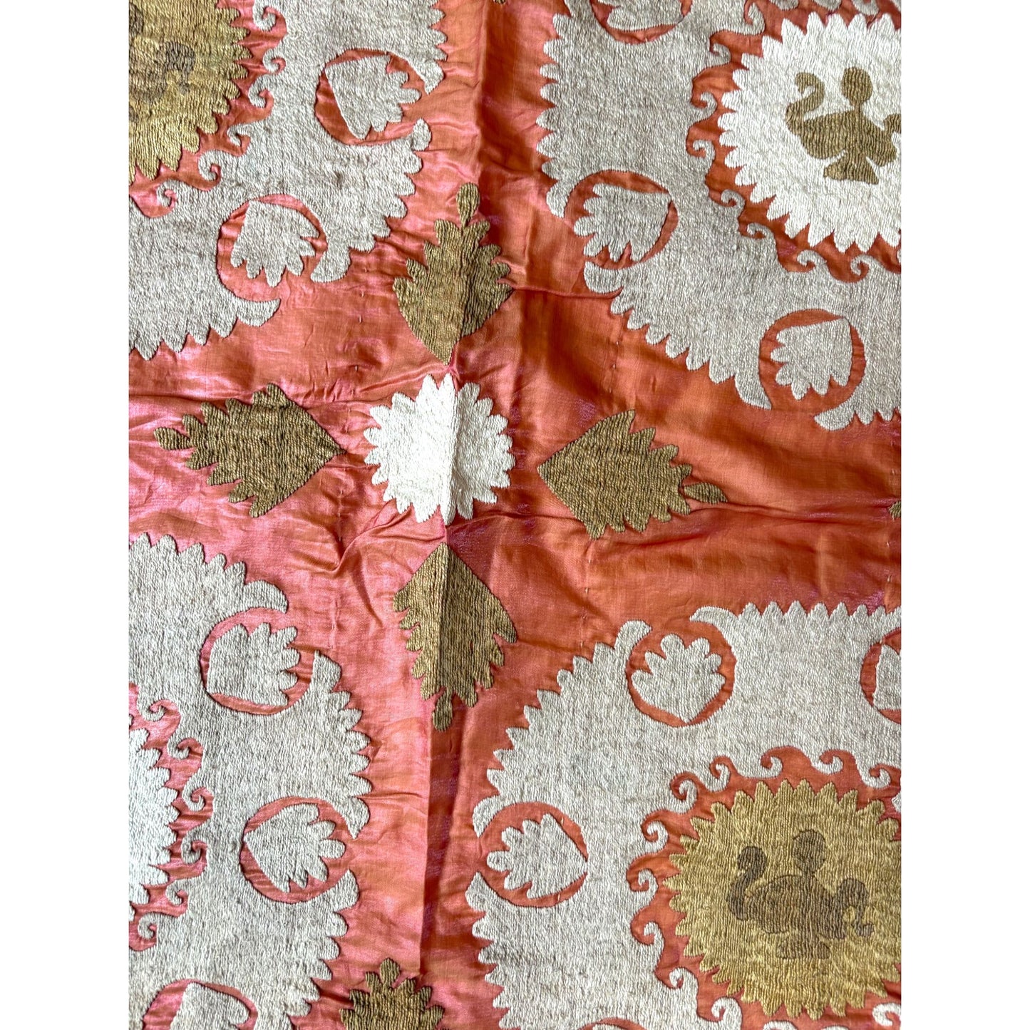 Close-up of a fabric with intricate white, gold, and red patterns on a white background