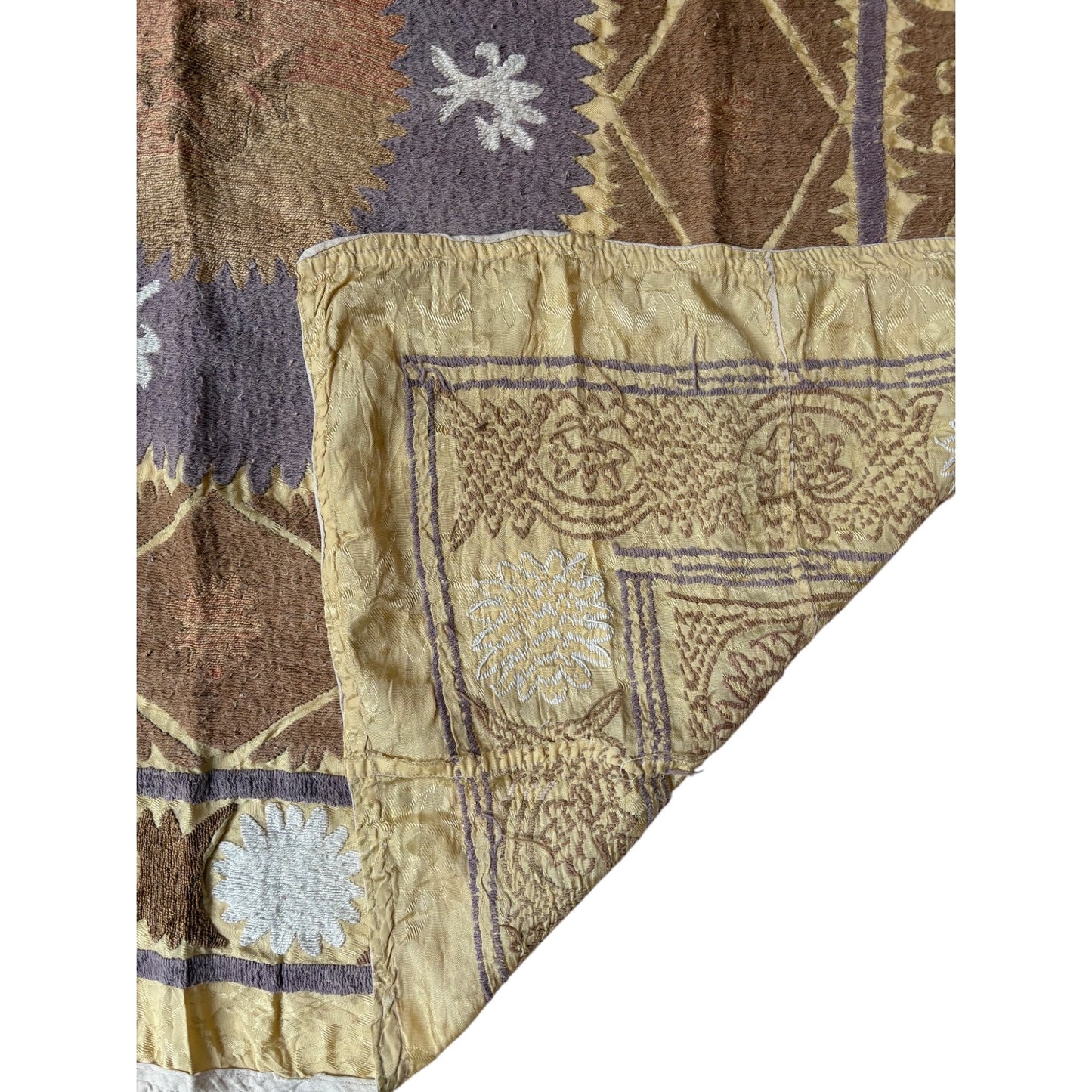 Close-up of a patterned fabric with embroidered designs in brown, purple, and beige.