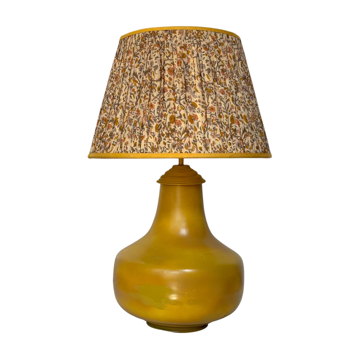 A vintage-style table lamp featuring a glossy mustard yellow ceramic base and a pleated fabric shade with a dense floral pattern in beige, brown, and muted orange tones.