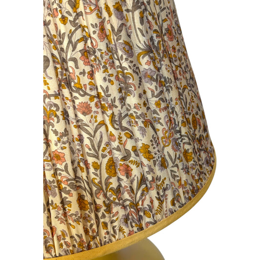 Close-up of the gathered silk lampshade with an intricate floral and botanical pattern in muted orange, yellow and brown on a cream background, finished with a yellow fabric border.