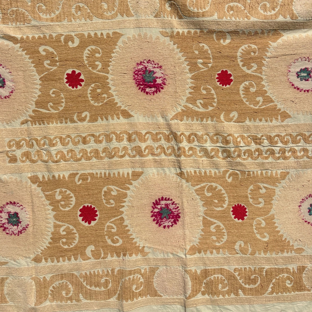 A close-up of a honey-gold and cream Suzani textile with woven floral motifs and red accents.
