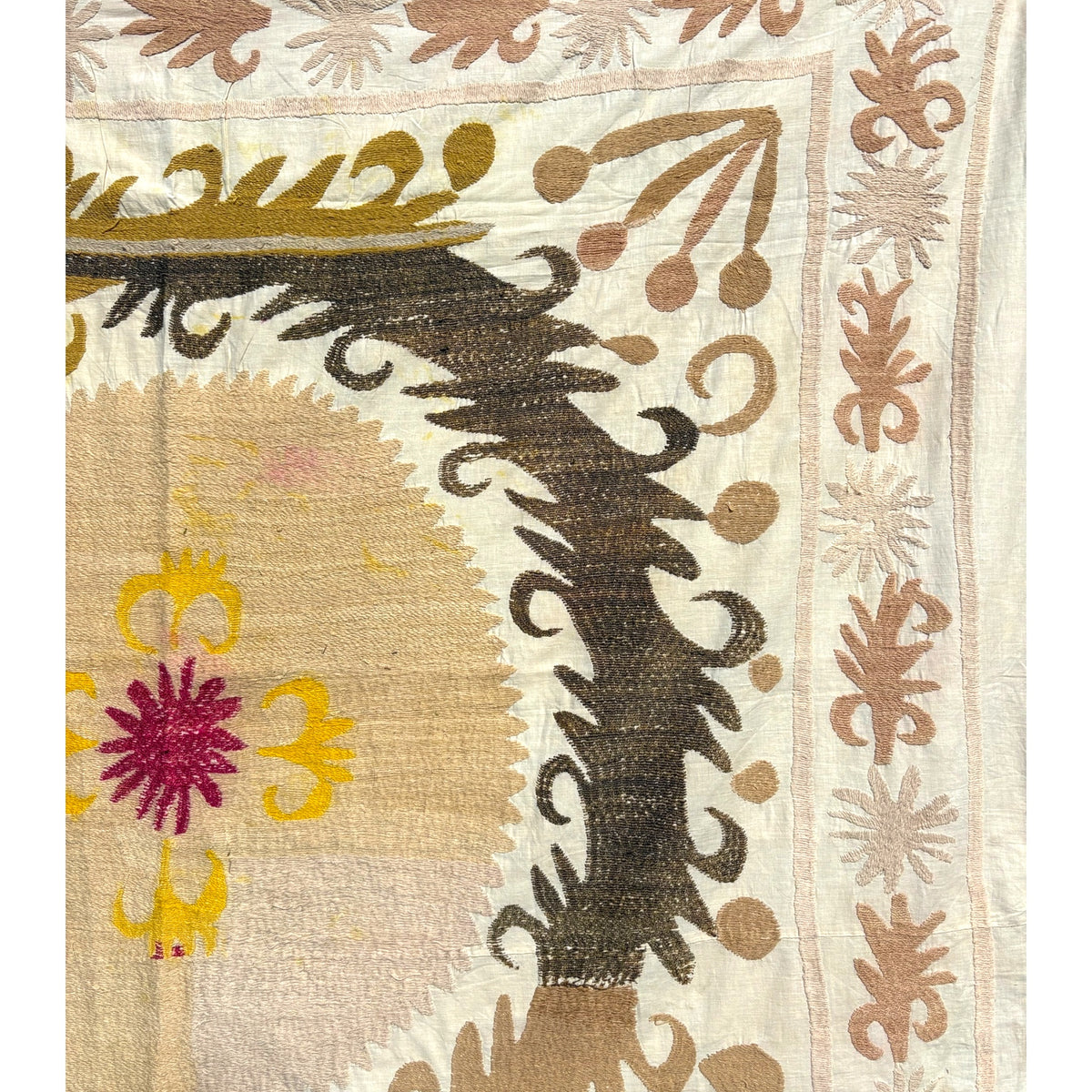 Close-up of hand-embroidered suzani showing a magenta flower with yellow curled motifs, dark brown feathery scrolls, and a leaf border