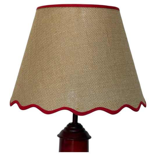Close-up of a natural hessian lampshade with a dark red scalloped trim, mounted on a dark reddish-brown wooden lamp base against a plain white background.