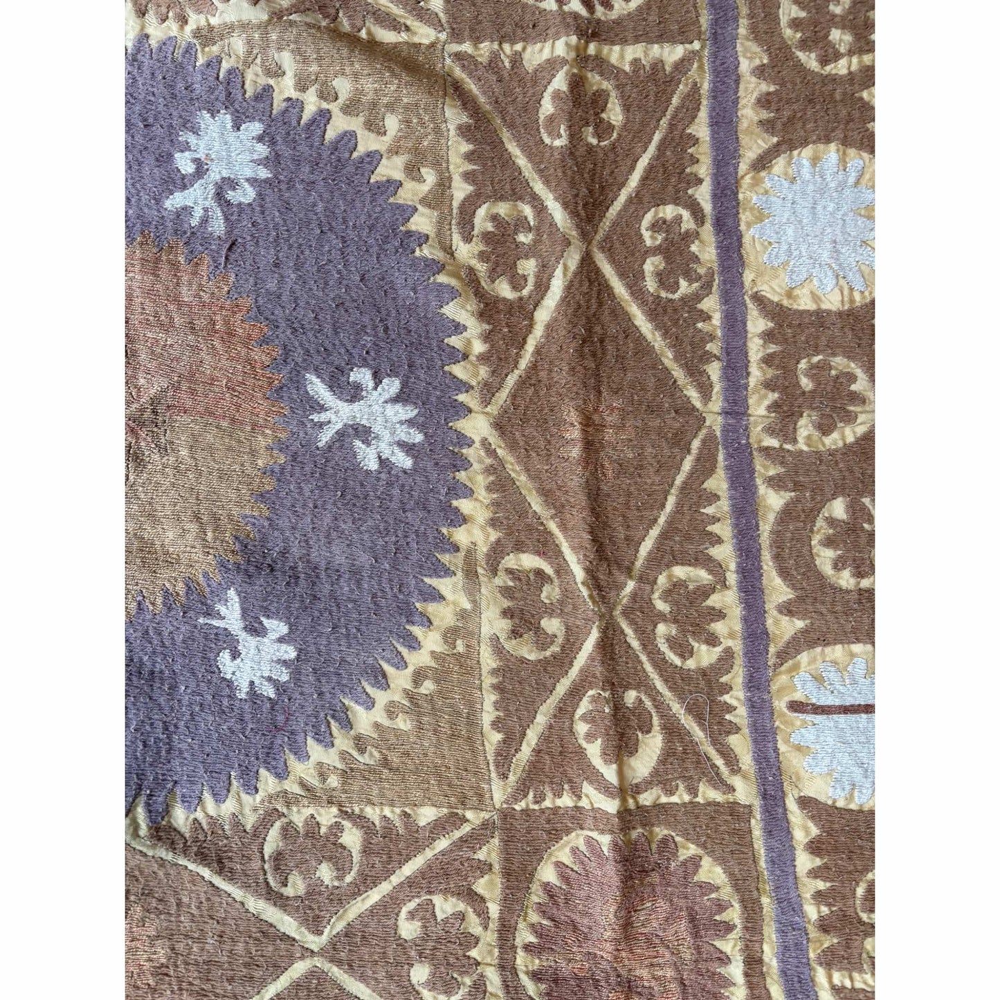 Close-up of a suzani fabric in brown, purple, and beige.