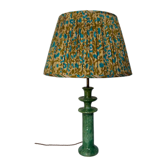 A table lamp with a gathered fabric shade featuring a blue and gold floral pattern, mounted on a textured green ceramic column base with a visible power cord.