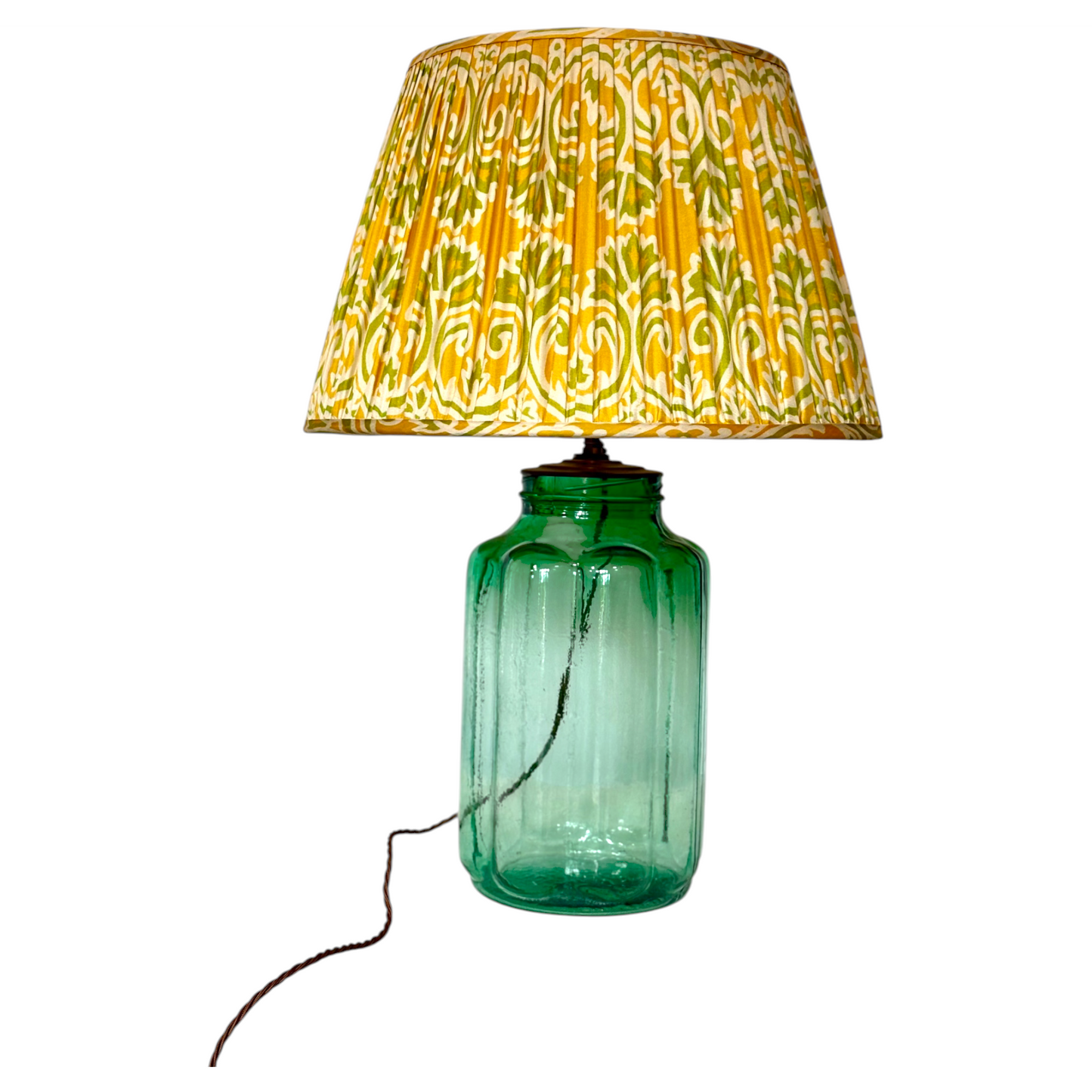 A gathered vintage silk sari lampshade with a yellow, green, and white paisley pattern shown on a green glass base.