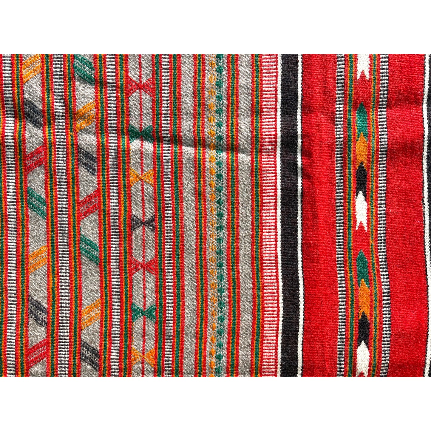 A close-up of a woven textile with vertical stripes and geometric patterns in red, gray, black, green, orange, and white.