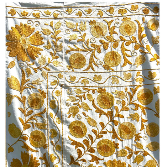 A close-up of the Suzani featuring an intricate golden-yellow floral and vine pattern.
