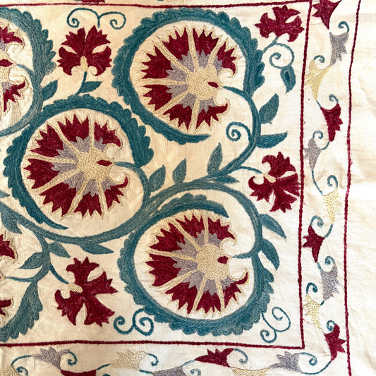 Detail of hand-stitched Suzani corner border with floral vine embroidery in burgundy and teal silk thread