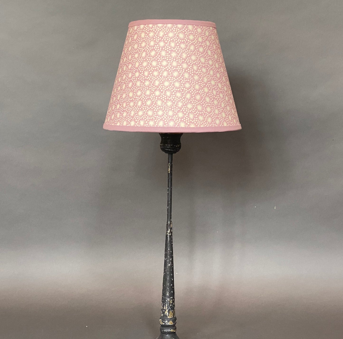 Pink Paper Lampshade shown on a tall candlestick lamp base on a grey background