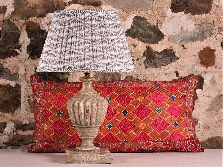 Grey Bangla Cotton Lampshade shown on a medium base with a bright red patterns cushion against a brick wall background