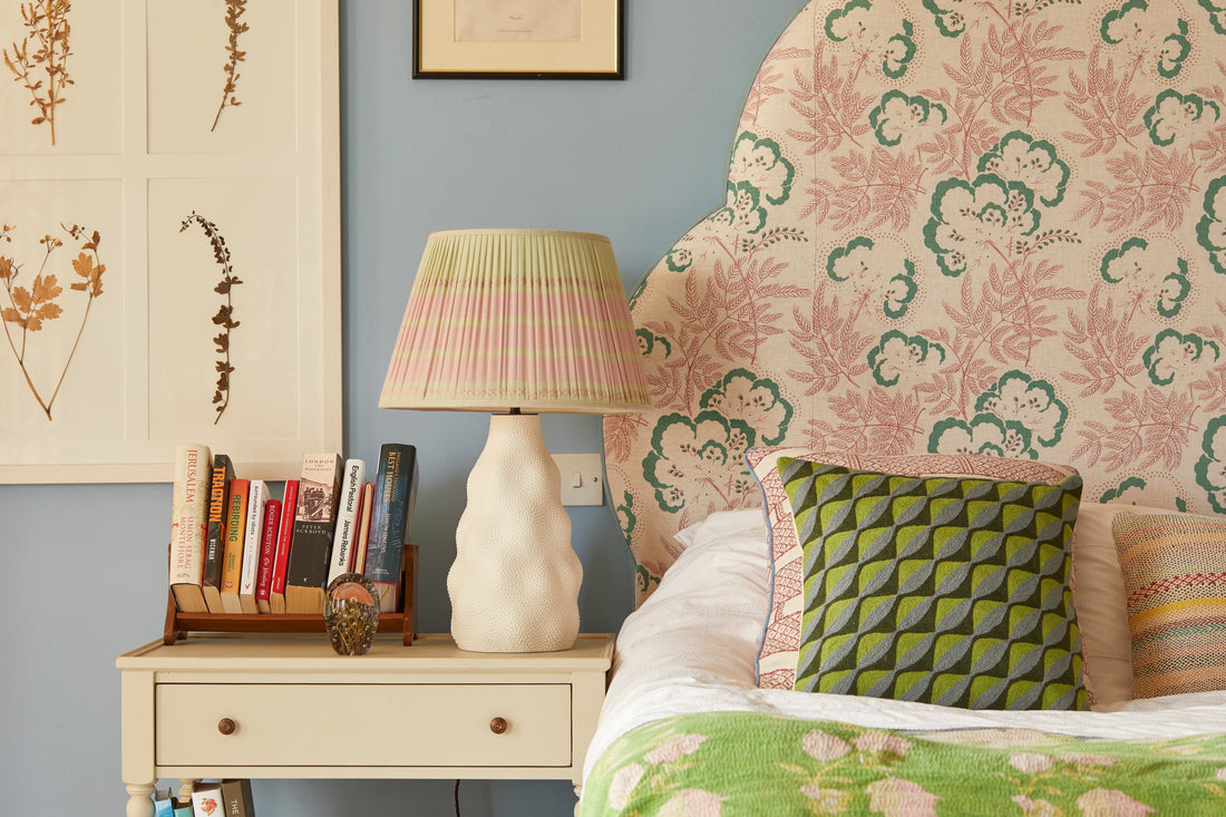 Green and Pink gathered lampshade on a white ceramic lampbase on a bedside table in a bedroom with a floral headboard 