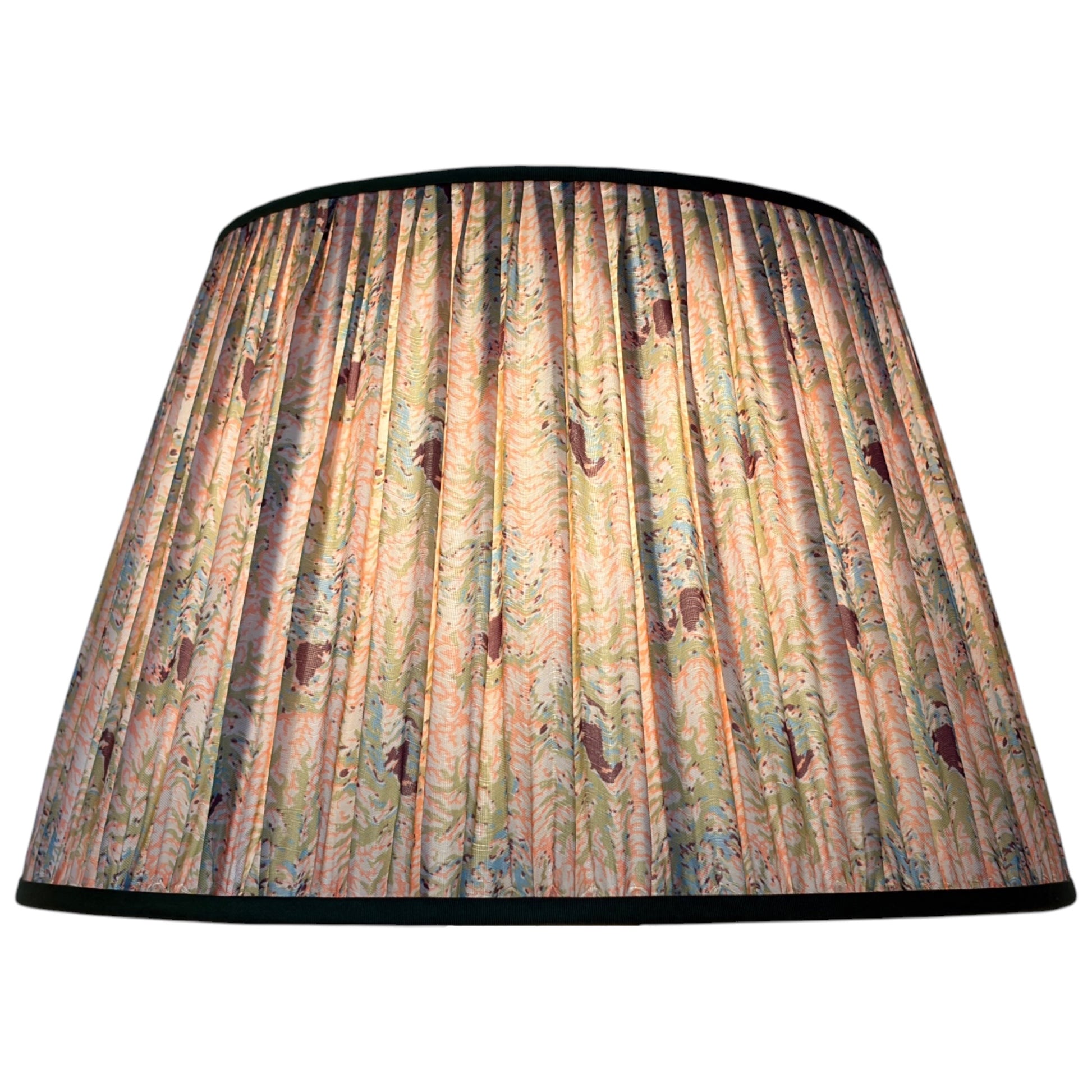 A gathered silk lampshade featuring a vintage coral and seaweed botanical pattern with green leaves, peach and pink flowers finished with olive green trim at the top and bottom with the light on. 