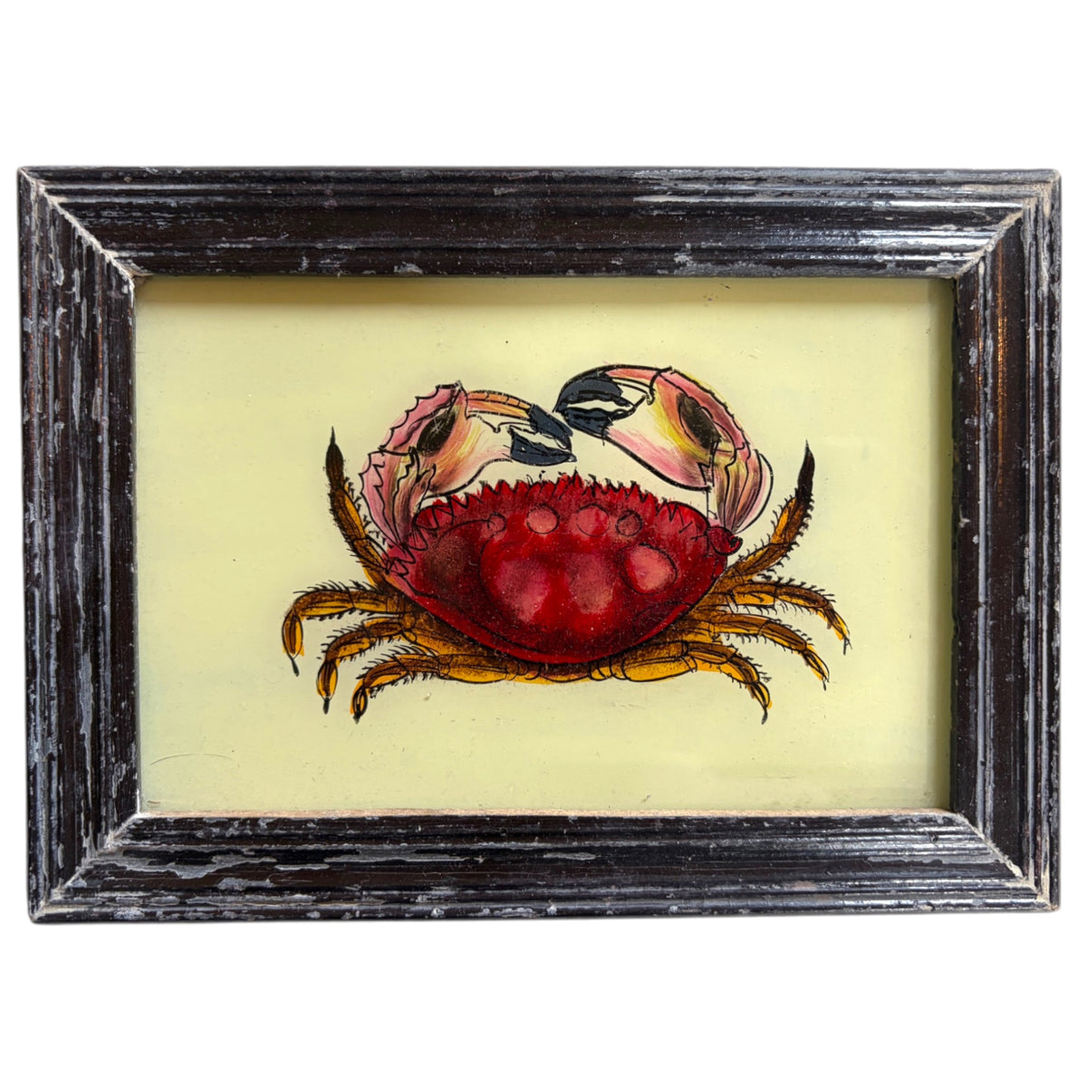 A framed art print featuring a painted red and pink crab on a pale yellow background, set in a distressed dark wood frame.