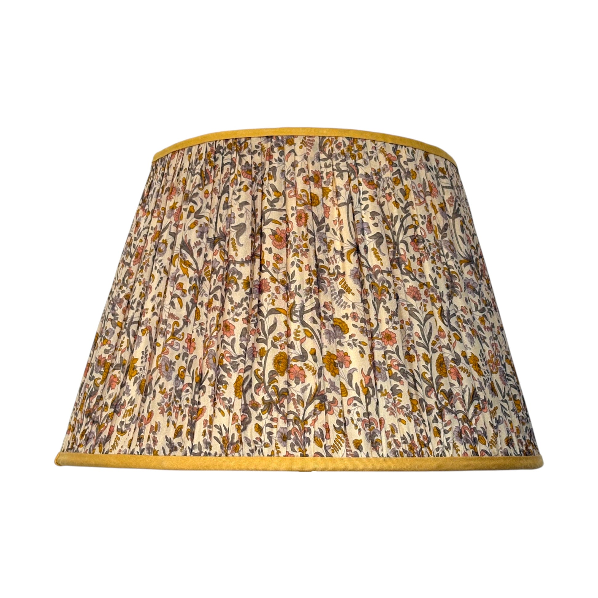 A gathered silk lampshade featuring an intricate vintage paisley floral and botanical pattern in muted tones of orange, yellow and brown on a cream background, finished with a contrasting mustard yellow trim.