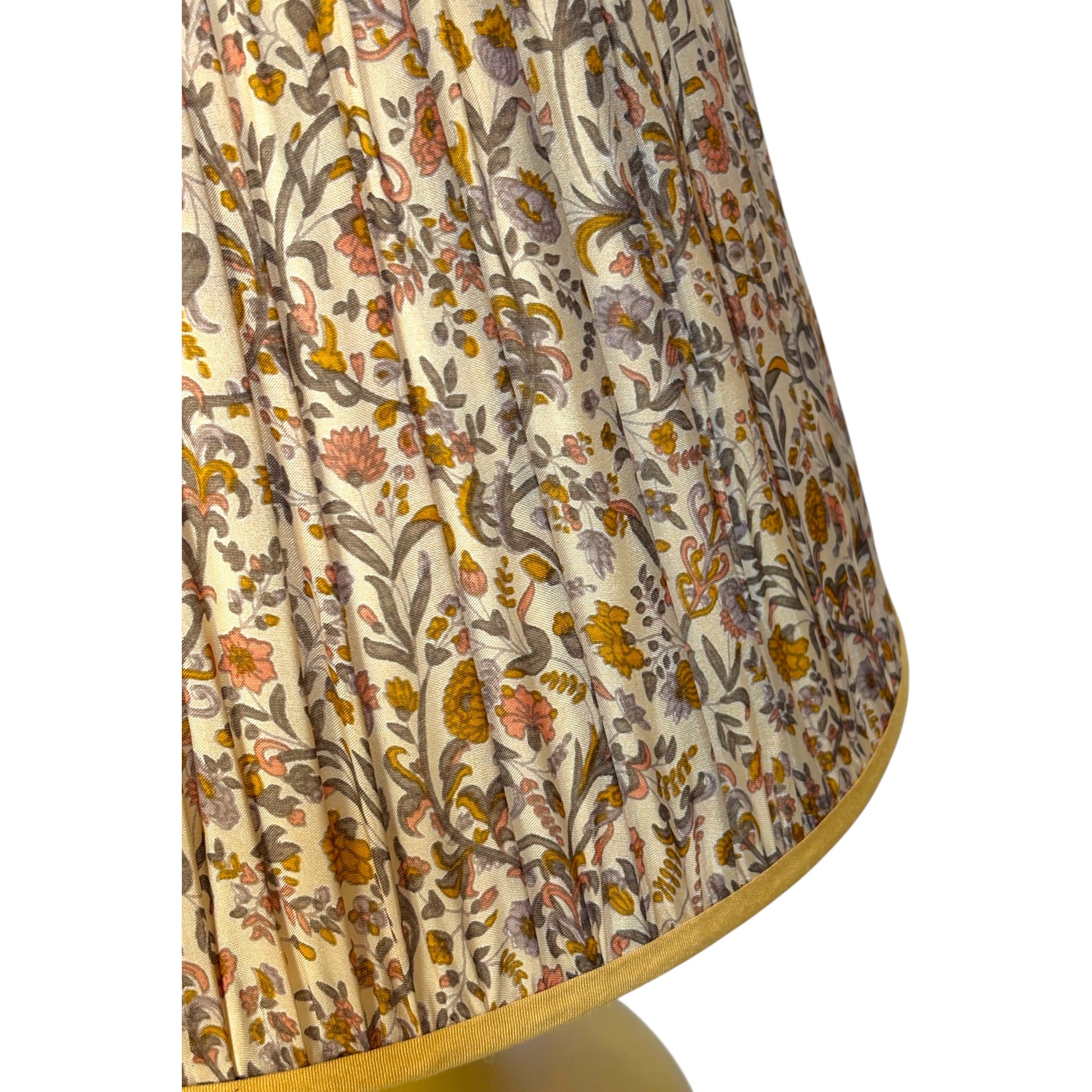 Close-up of the gathered silk lampshade with an intricate floral and botanical pattern in muted orange, yellow and brown on a cream background, finished with a yellow fabric border. 