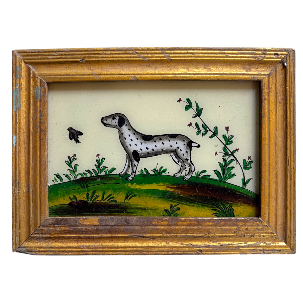A framed vintage-style painting depicting a spotted dog standing on a green hill with plants and a small bird, enclosed in an ornate distressed gold frame against a white background.