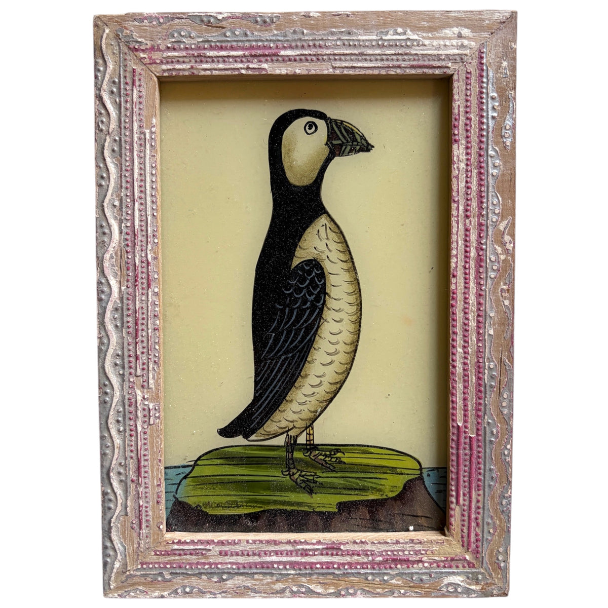 A framed vintage-style illustration of a puffin standing on a green rock against a pale yellow background, enclosed in an ornate distressed silver and pink frame.