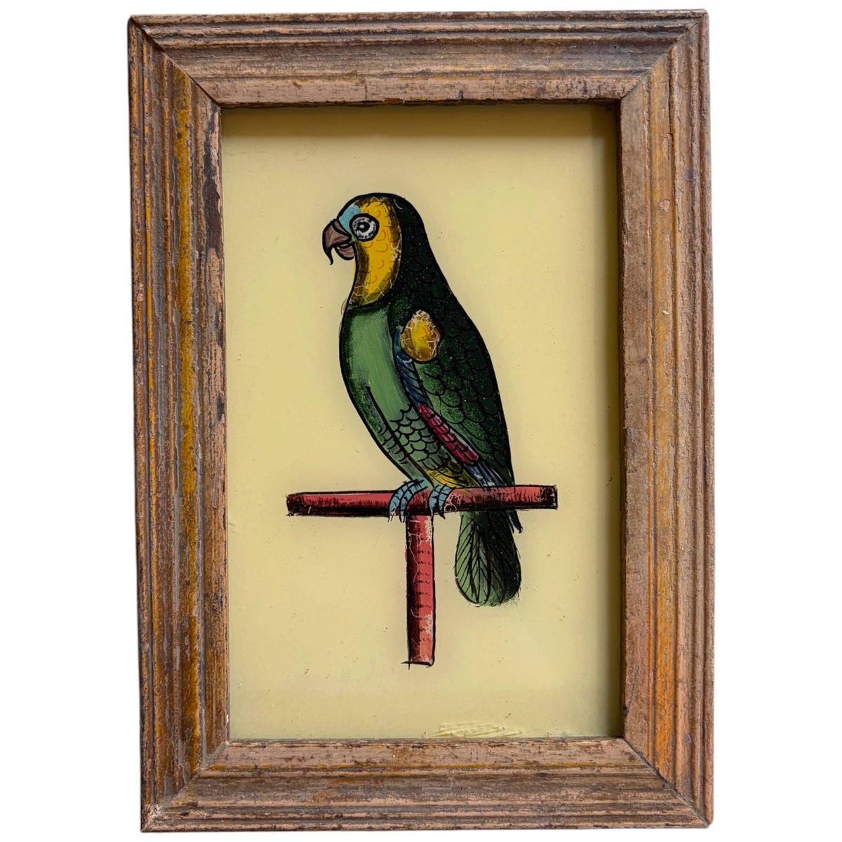 A framed vintage-style illustration of a green and yellow parrot perched on a red crossbar, set against a pale yellow background and enclosed in a rustic brown wooden frame.