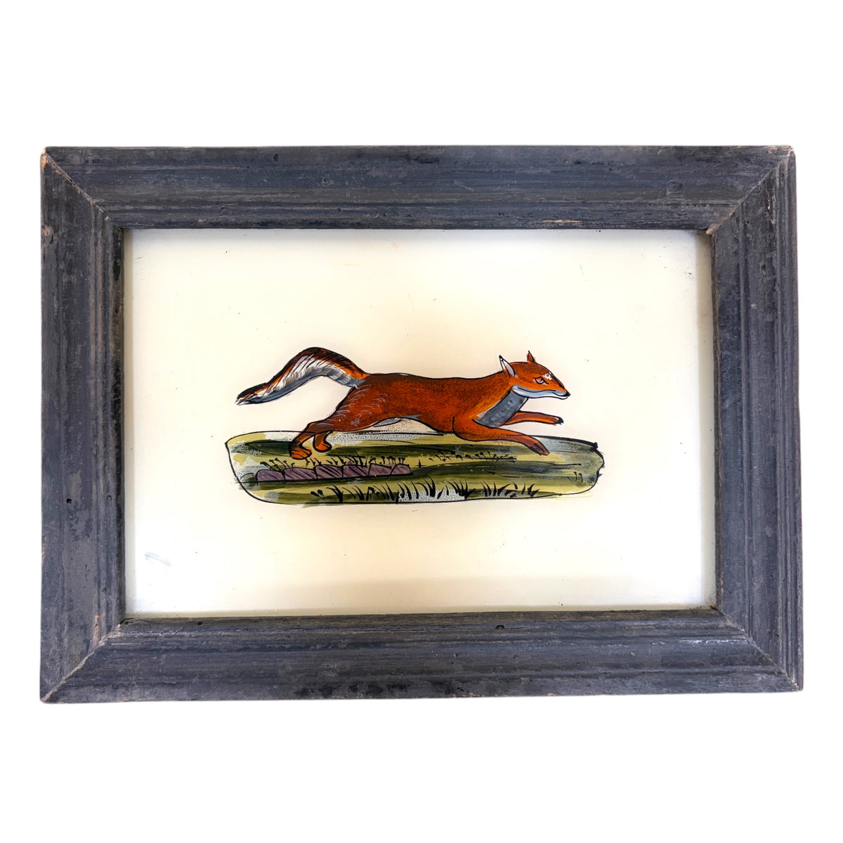 a russet fox with a white-tipped tail, caught mid-stride across a grassy bank. Distressed grey wooden frame.
