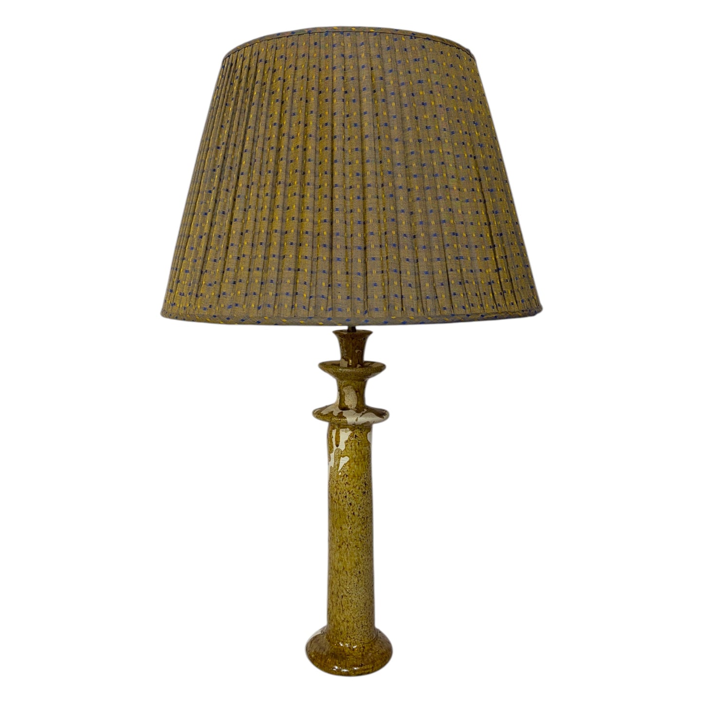 A Tamegroute table lamp, textured, speckled column base in a warm ochre and cream colour, isolated on a white background.