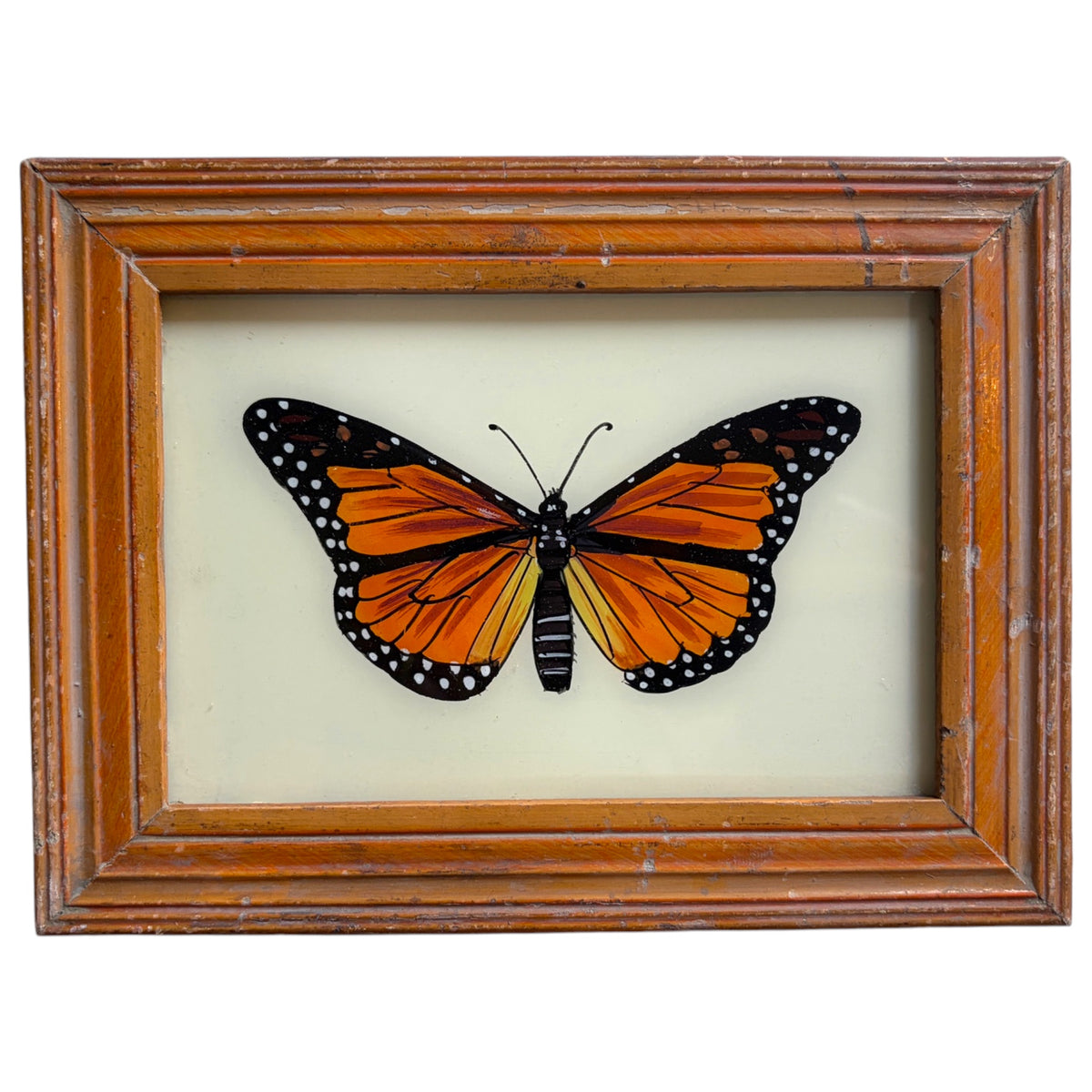 A framed butterfly artwork featuring a monarch butterfly with orange, black, and white wings, mounted inside a distressed brown wooden frame on a light cream background.