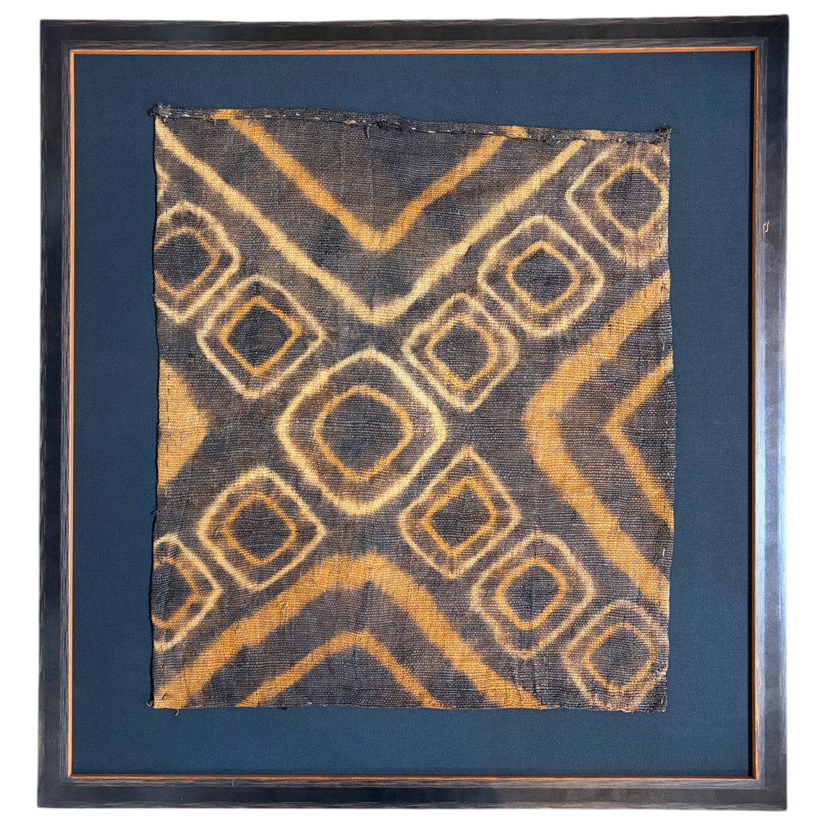 A framed textile art piece featuring a central square fabric panel with a geometric diamond pattern in ochre yellow and dark charcoal, surrounded by a black mount and a rustic dark wood frame. Slight scratch on frame. 