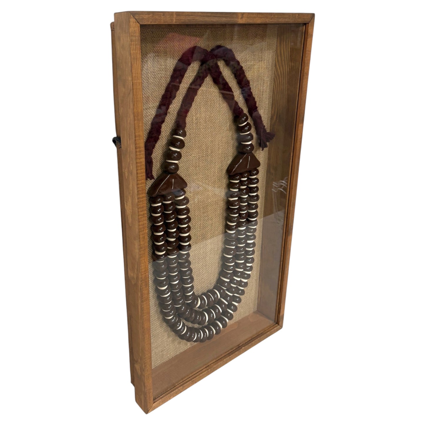 A beaded necklace displayed inside a wooden shadow box frame with a clear glass front, set against a plain white background.