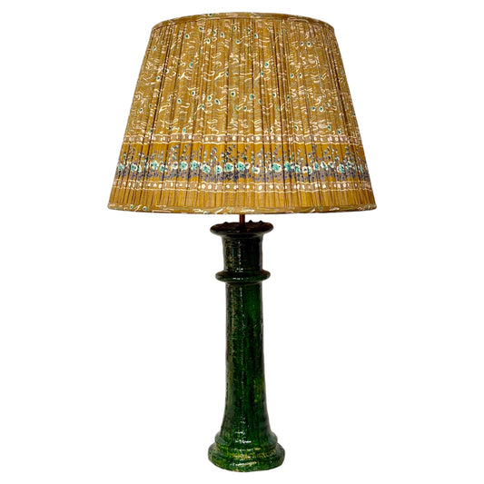 A green ceramic table lamp with a pleated vintage silk sari lampshade, isolated on a white background.