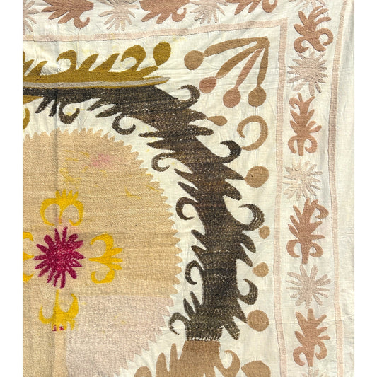 Close-up of hand-embroidered suzani showing a magenta flower with yellow curled motifs, dark brown feathery scrolls, and a leaf border