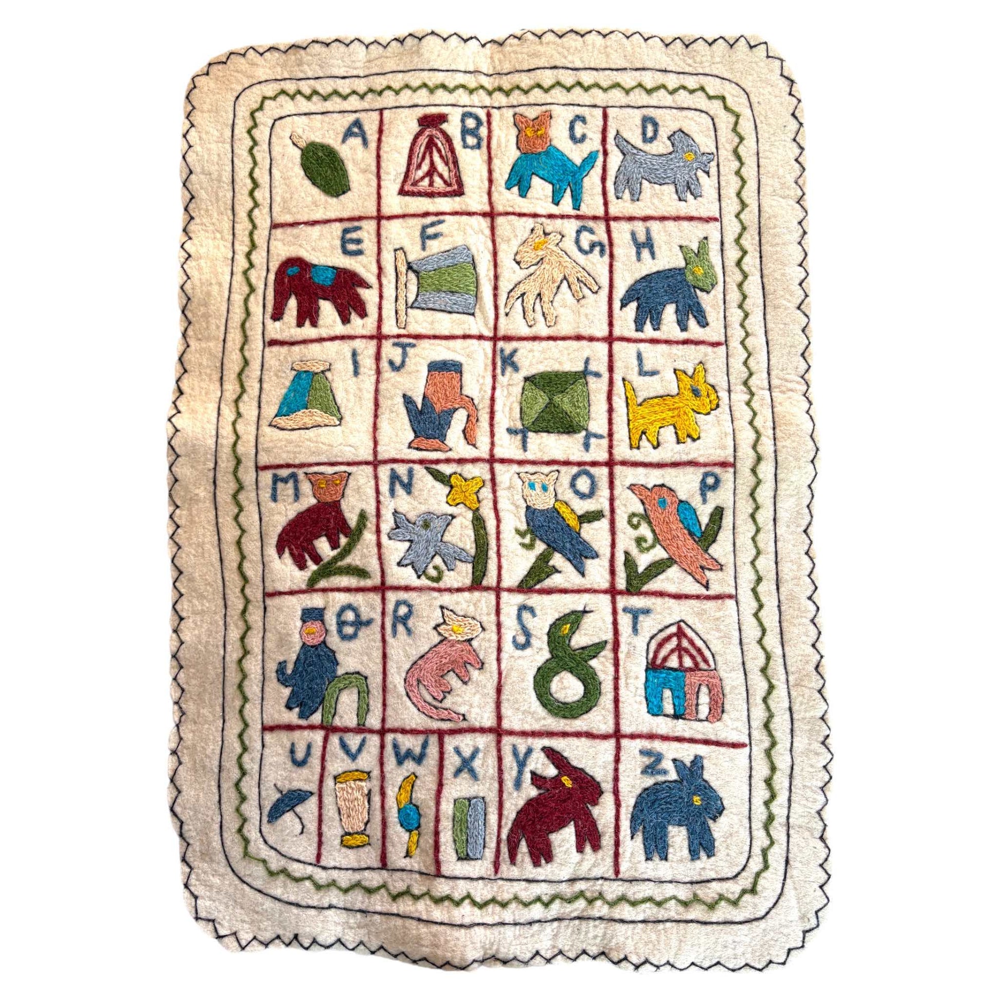 Alphabet wall hanging, showing a Namda technique. Cream wool with colourful embroidery on a white background. 