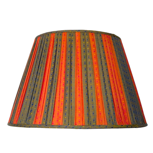 A gathered cotton fabric lampshade featuring vertical stripes of orange and green with small yellow, blue and red dotted accents, shown against a plain white background.