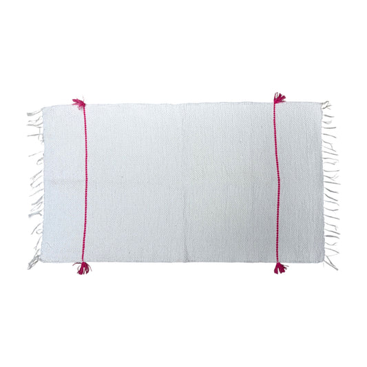 A white woven bath mat with fringe on the short ends and two vertical magenta-pink stitched stripes with tassels, shown flat against a white background.