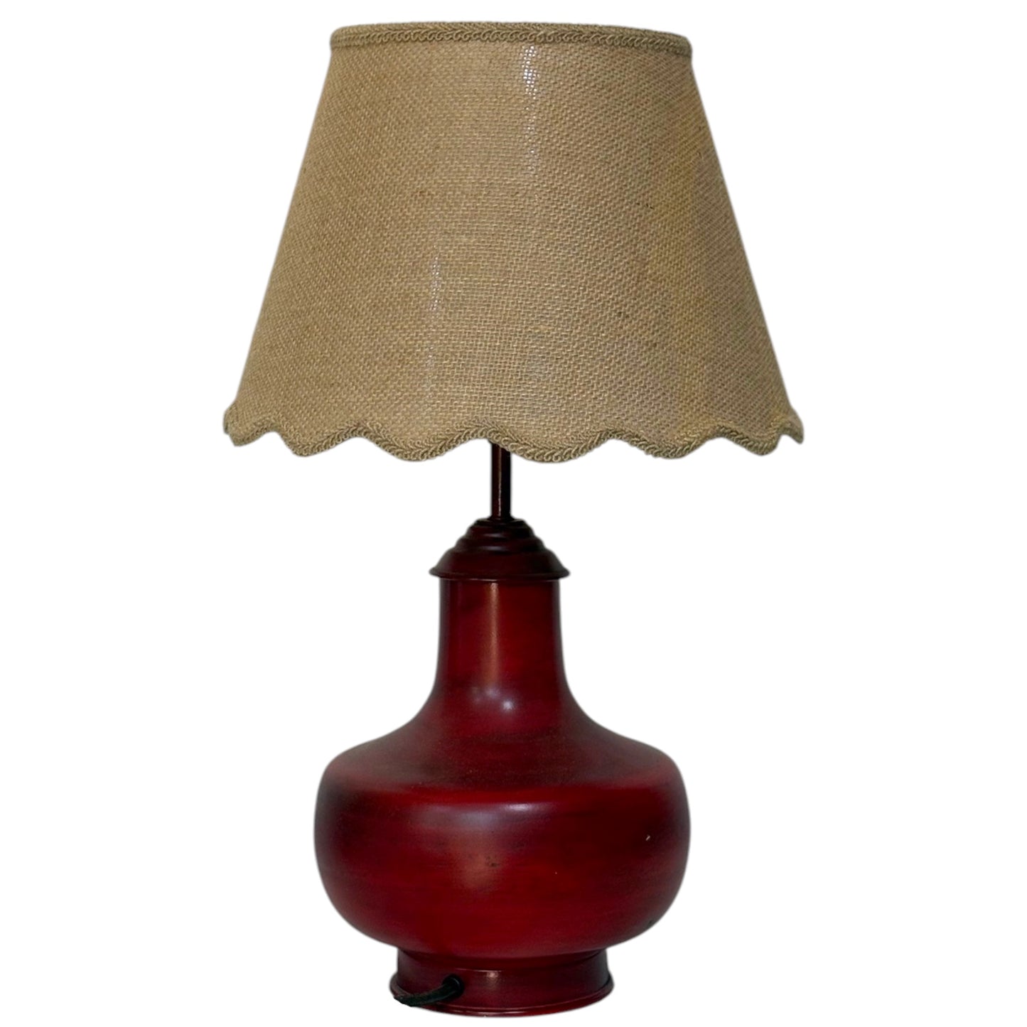 A table lamp featuring a glossy dark red ceramic bulb base and a natural beige hessian lampshade with a scalloped edge.