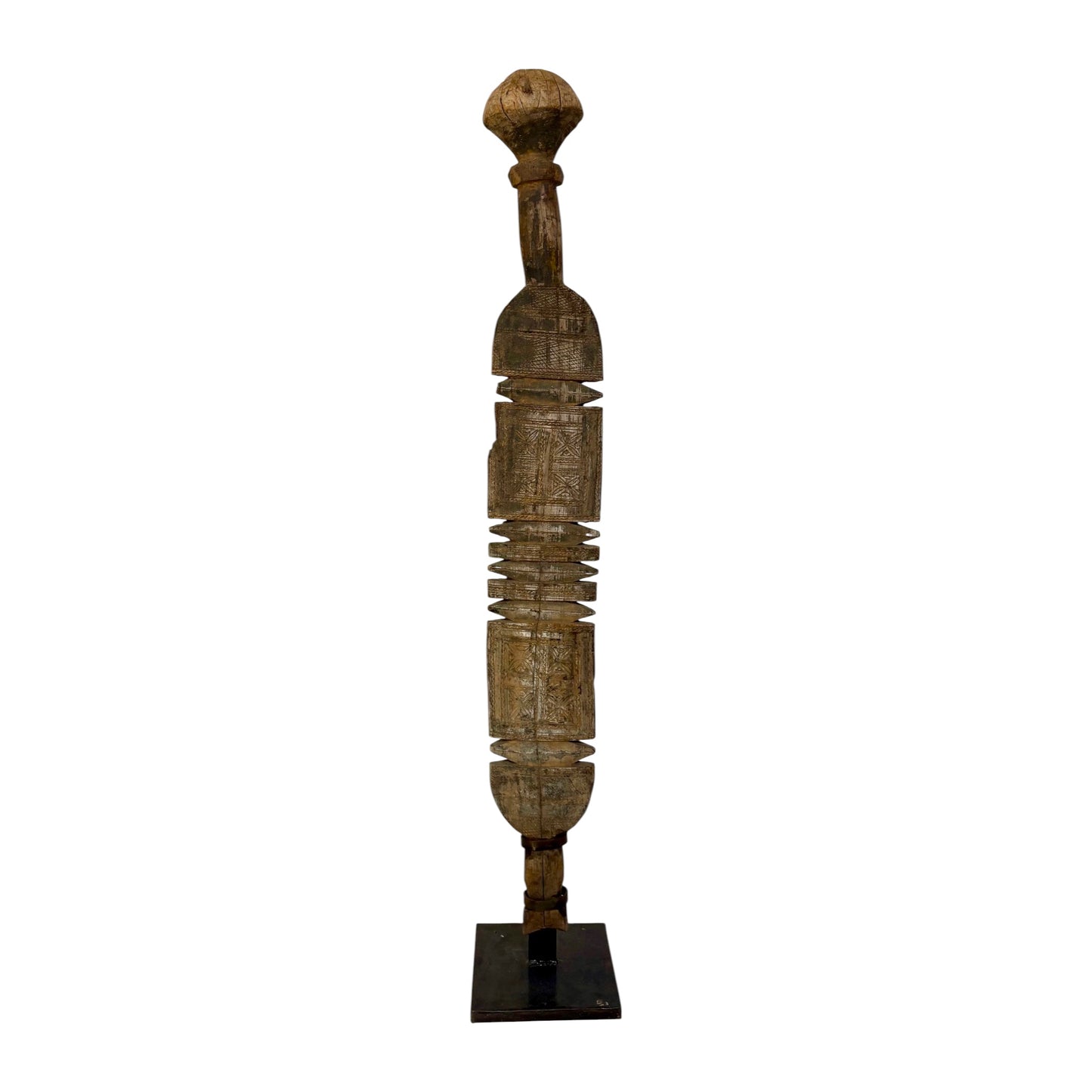 A tall, slender carved wooden sculpture with a rounded top and a dark rectangular base, photographed against a plain white background.