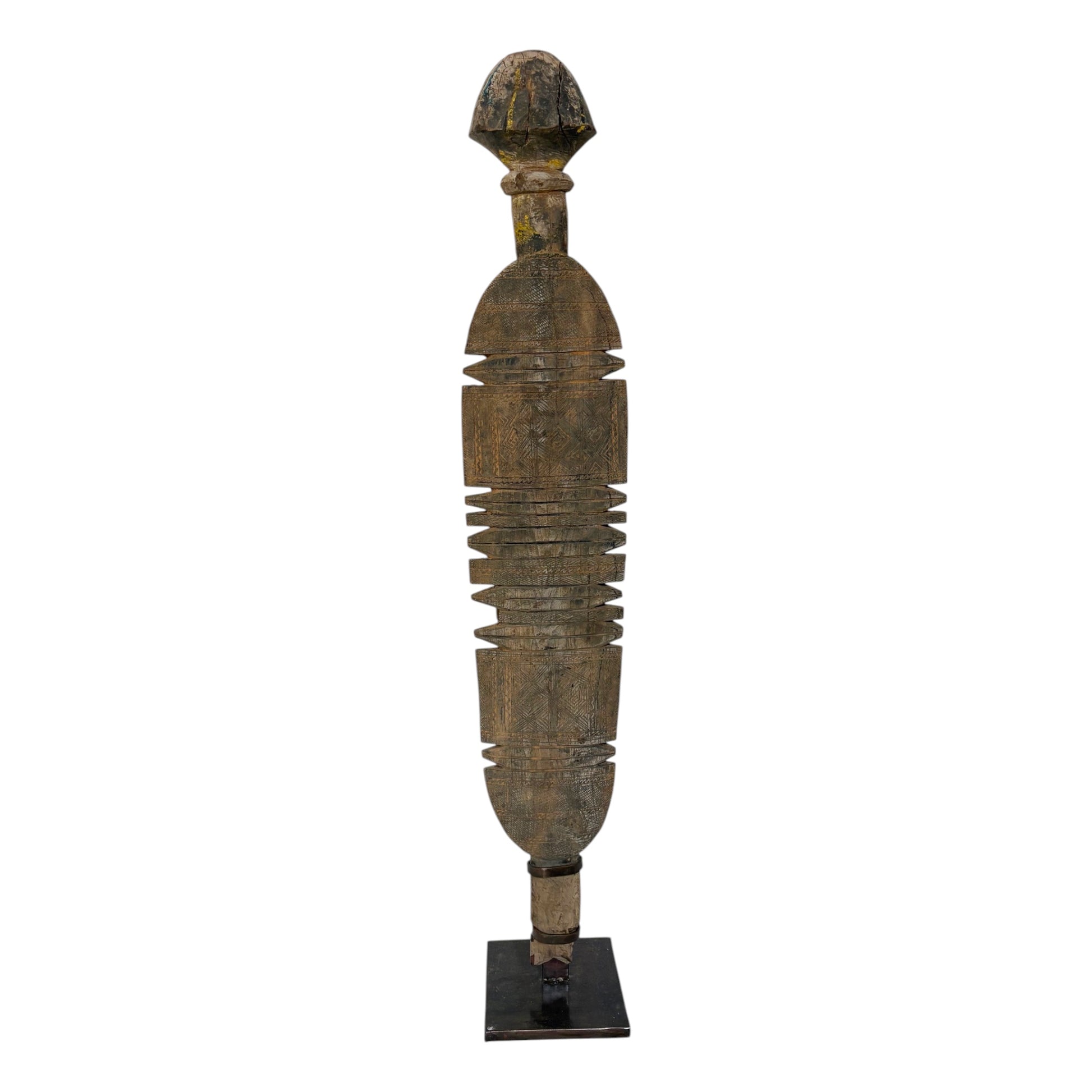 A tall, narrow carved wooden decorative sculpture with a weathered brown and black finish, standing on a small black base against a plain white background.