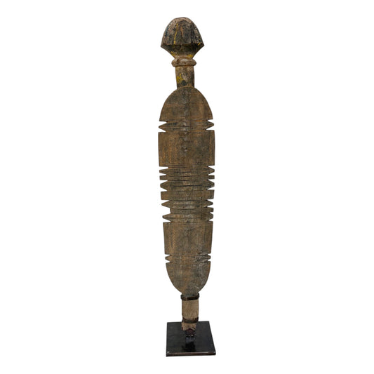 A tall, narrow carved wooden decorative sculpture with a weathered brown and black finish, standing on a small black base against a plain white background.