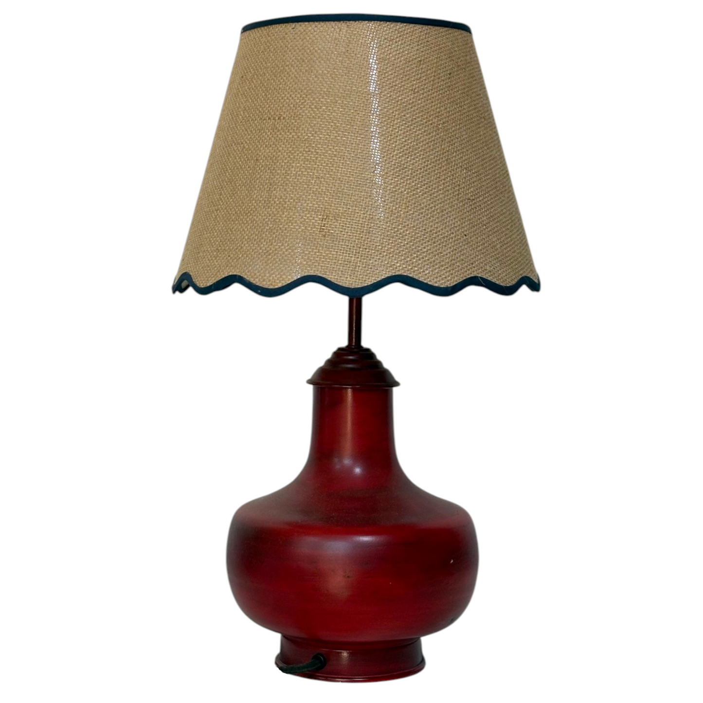A table lamp with a glossy dark red ceramic or glass bulb-shaped base and a beige hessian lampshade with a dark blue scalloped edge, isolated on a white background.