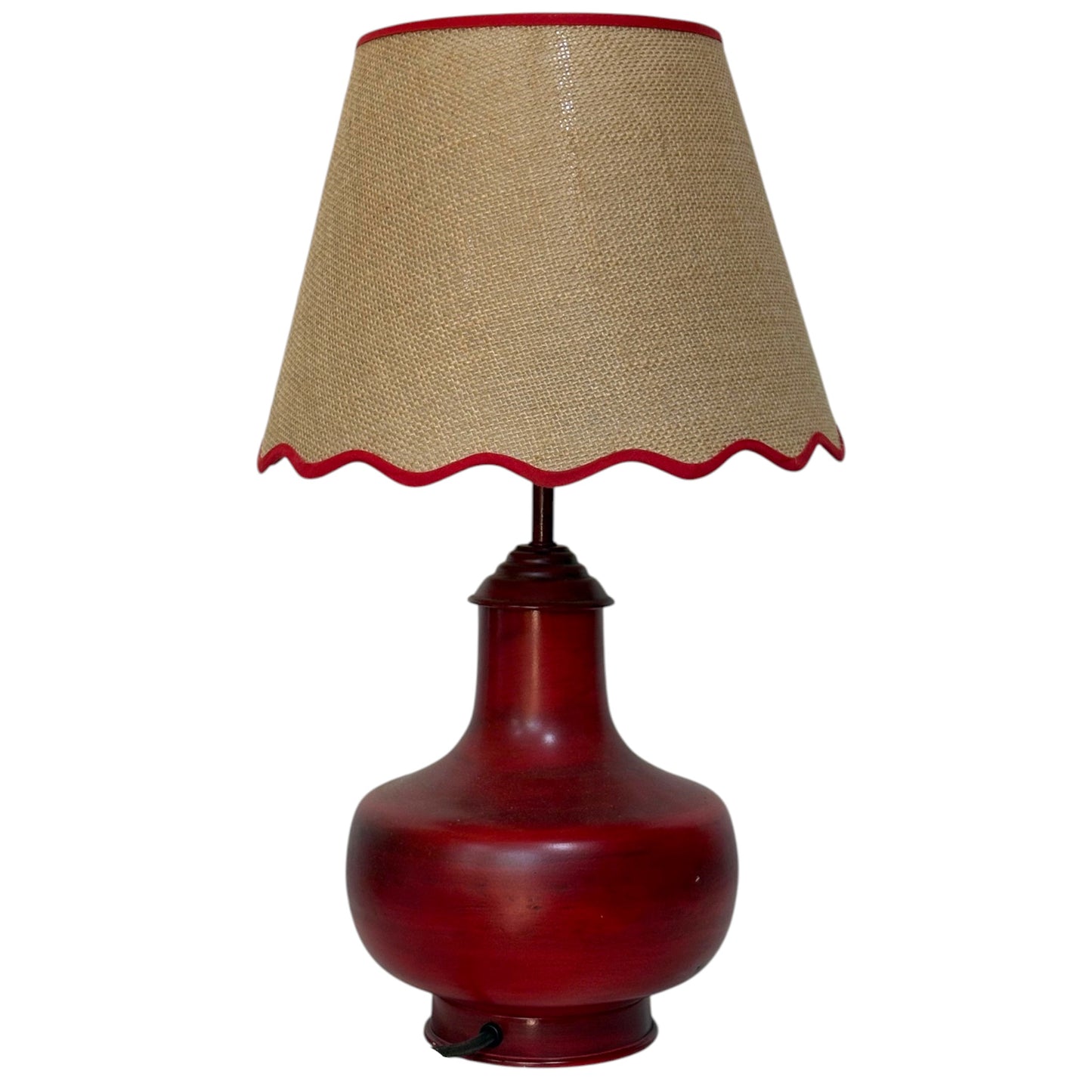 A table lamp with a glossy dark red ceramic base and a beige hessian shade trimmed with a scalloped edge in red fabric.