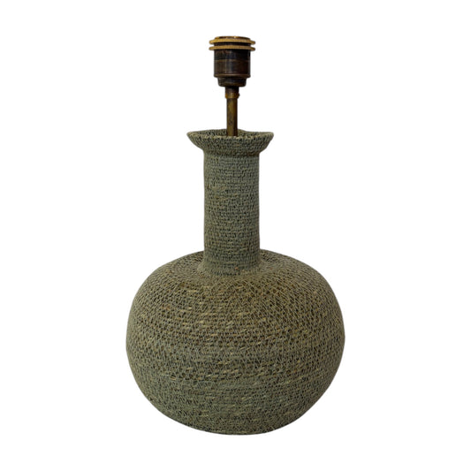 A decorative table lamp with a round, bulb-shaped base and a tall, narrow neck, both covered in a textured woven material in a muted olive green color. The lamp features a brass-toned metal socket at the top, set against a plain white background.