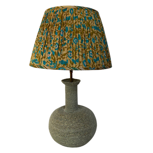 A table lamp with a textured gray-green woven base and a pleated drum shade featuring a mustard yellow and teal floral pattern, shown against a plain white background.