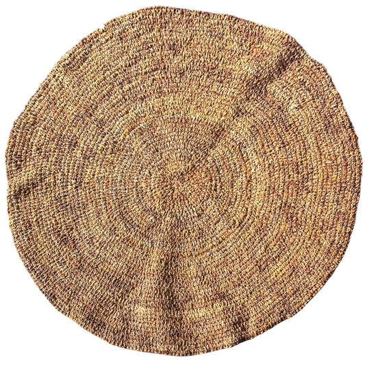 A round, hand-woven natural fiber rug in a textured tan and brown color palette, shown from a top-down perspective on a solid white background.
