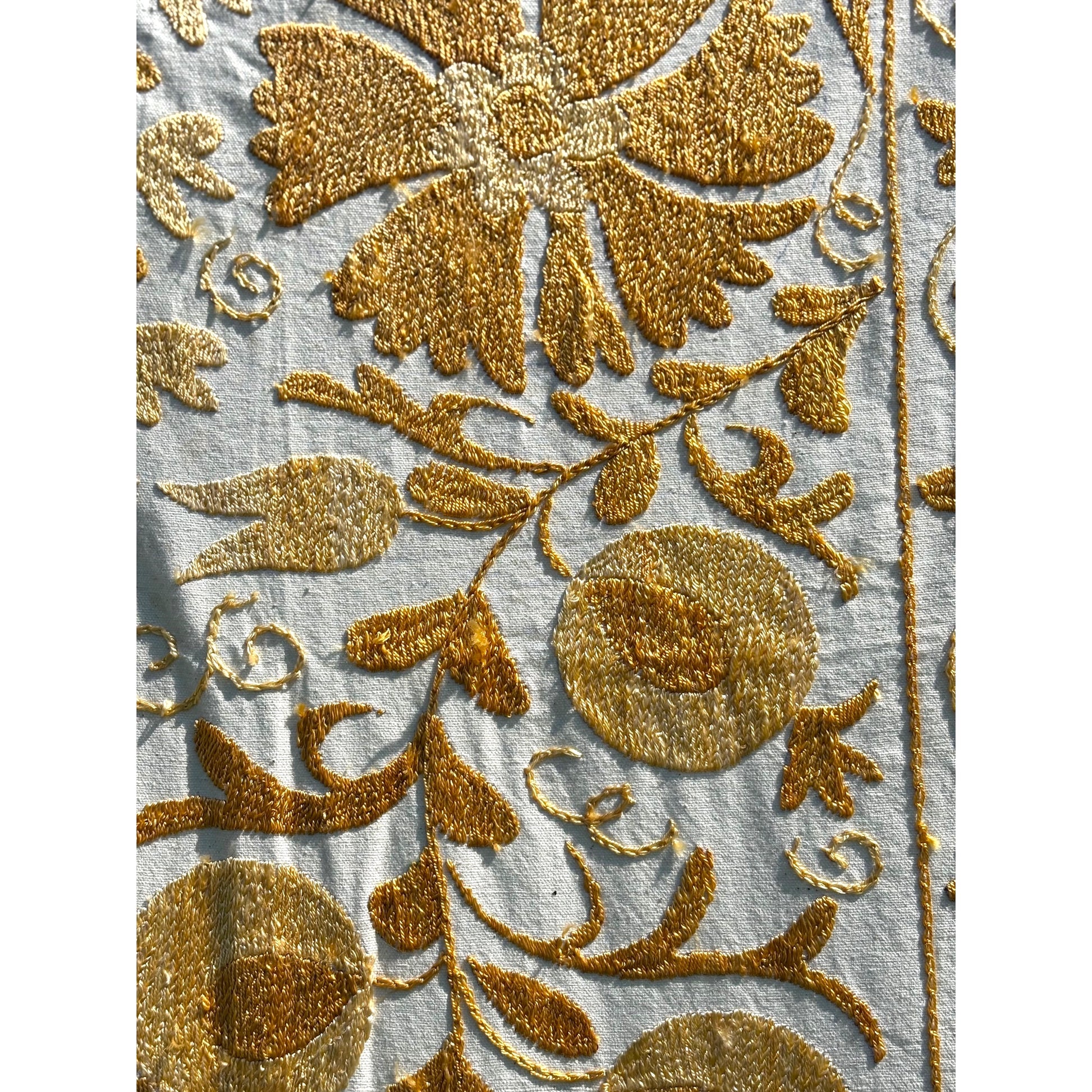 A close-up of a Suzani featuring a yellow floral and vine embroidery. 