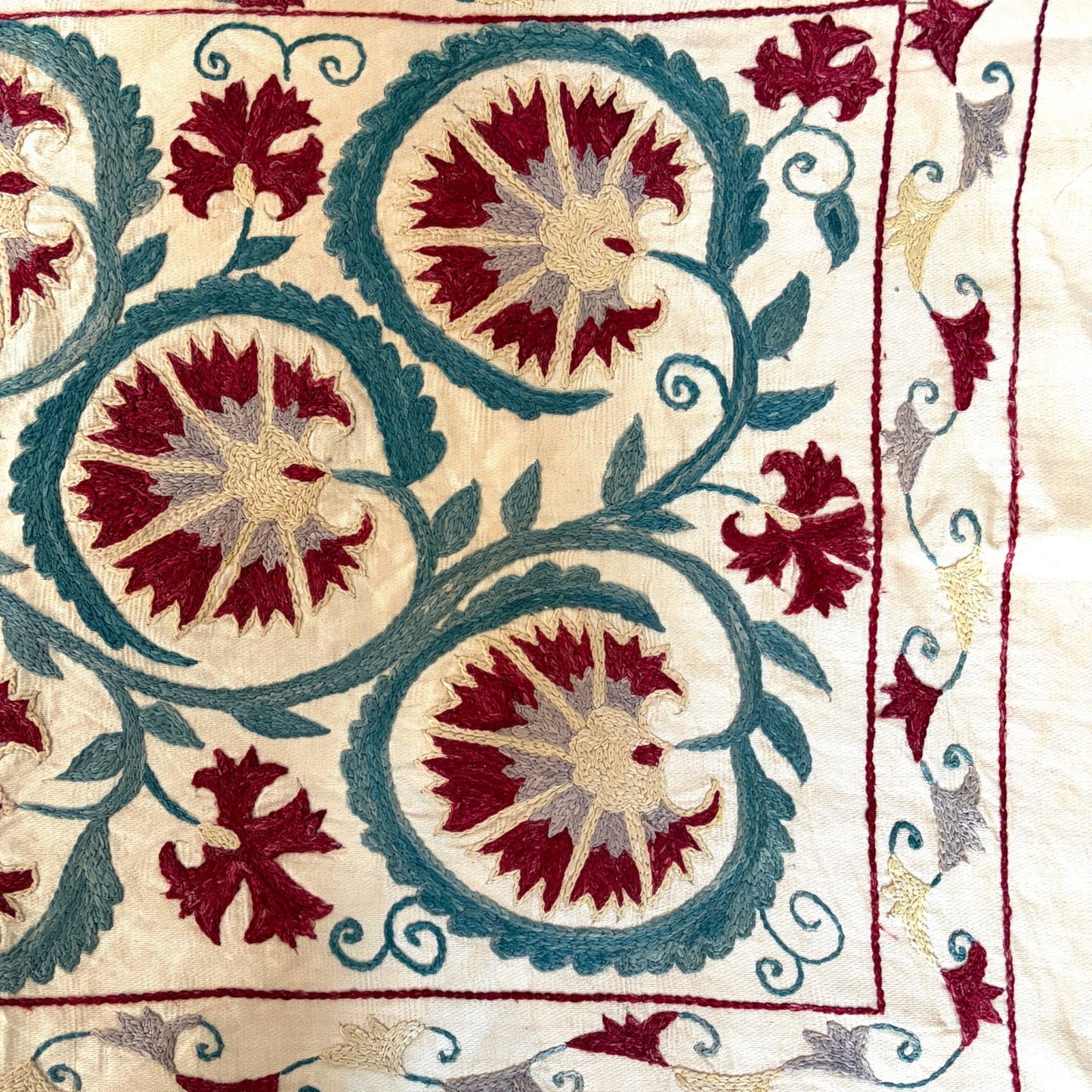Detail of hand-stitched Suzani corner border with floral vine embroidery in burgundy and teal silk thread