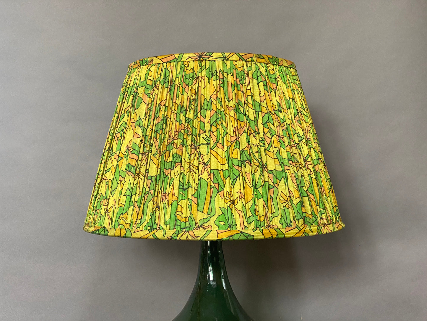 Green & citrine silk lampshade shown on a bottle green glass lamp base and a grey background