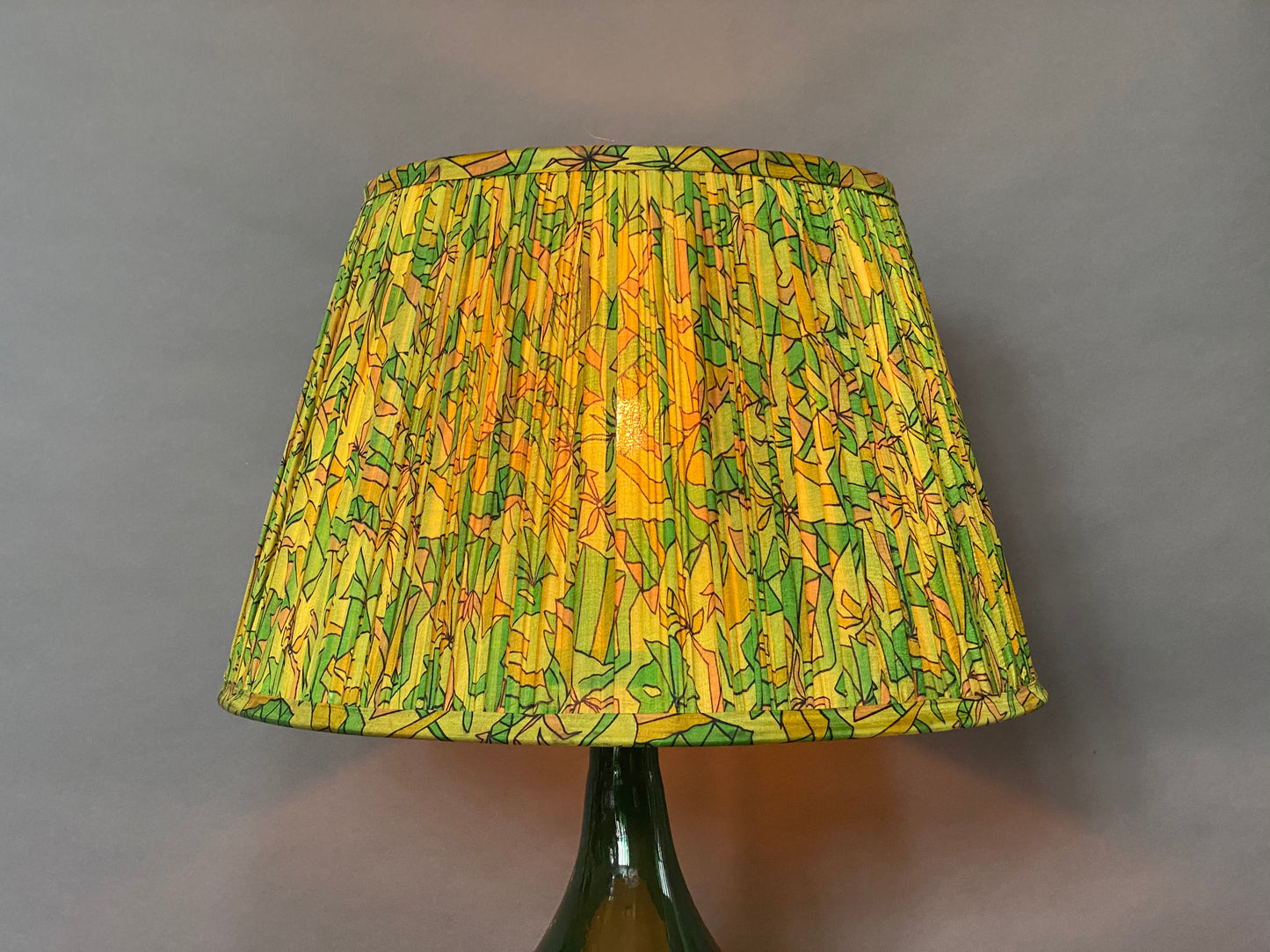 Green & citrine silk lampshade shown lit on a grey background