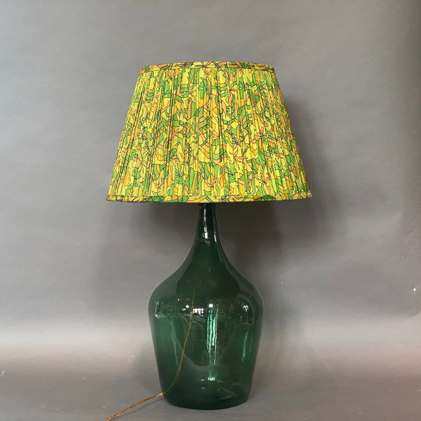 Green & citrine silk lampshade sown on a bottle green glass lamp base on a grey background
