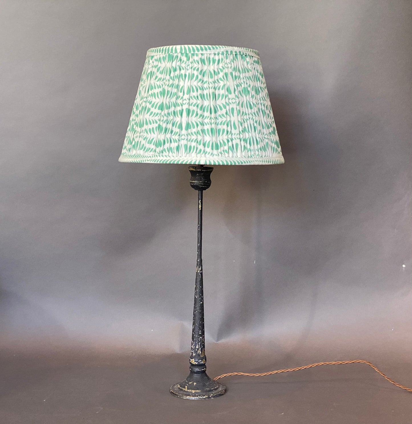 Green Bangla Cotton Lampshade shown on a rustic candlestick lamp base on a grey background