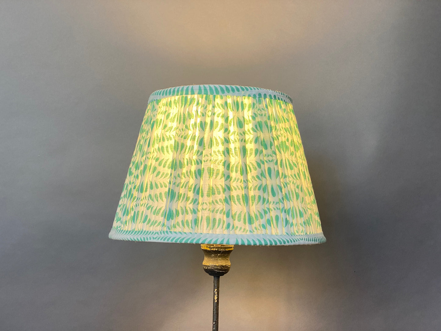 Green Bangla Cotton Lampshade shown lit on a grey background