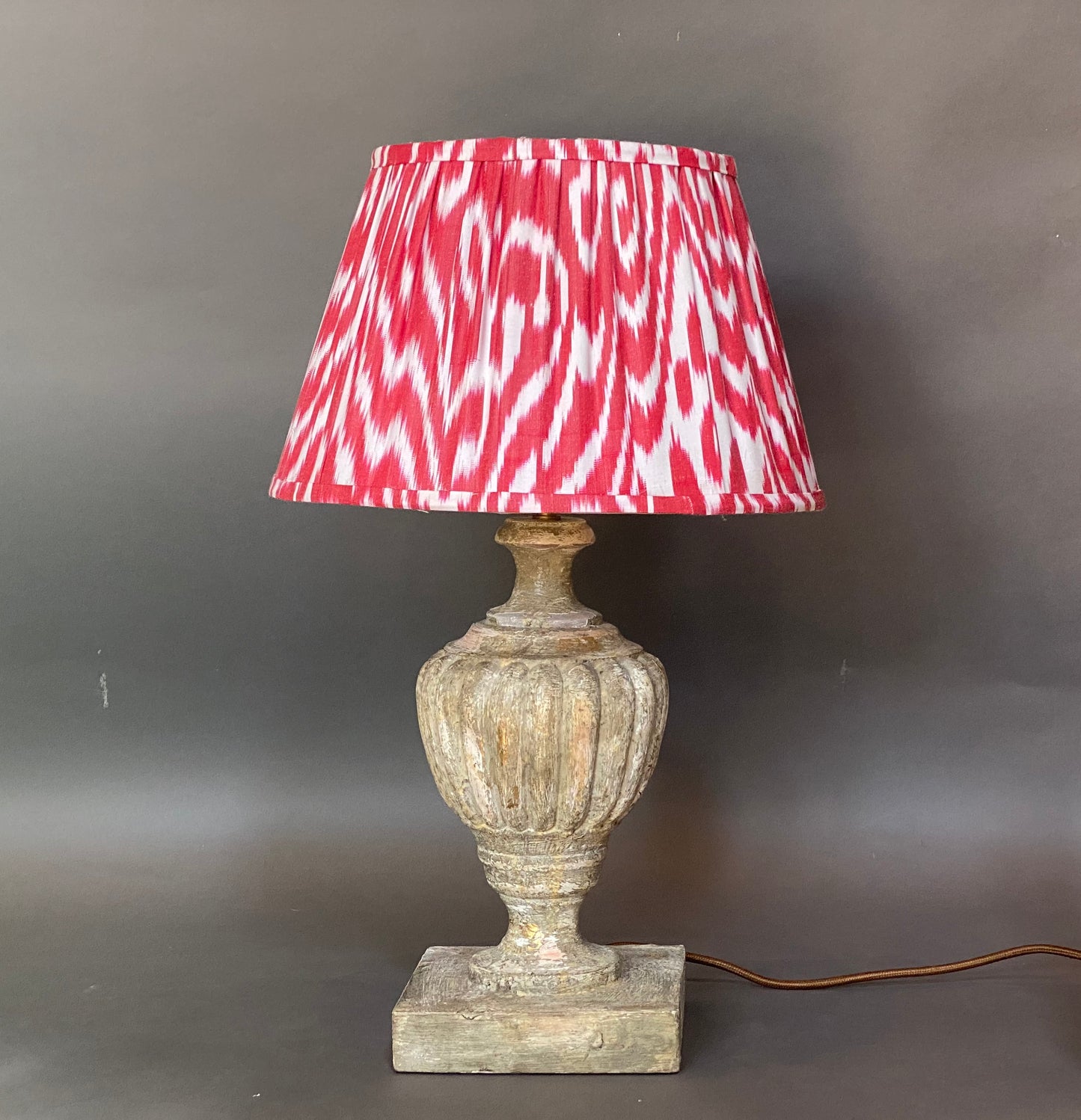 Red and white ikat silk lampshade shown on an urn lamp base with a grey background
